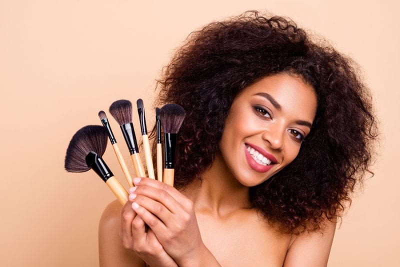 mulher negra segura pincéis de maquiagem e sorri