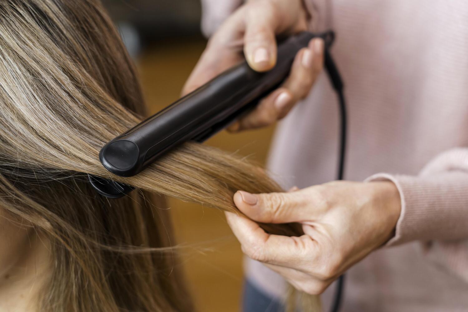 cloese de uma mulher passando chapinha em um cabelo loiro